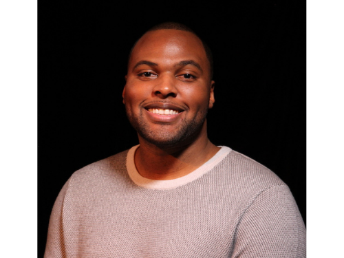Tarig Male African American high school graduate smiles at the camera, black background