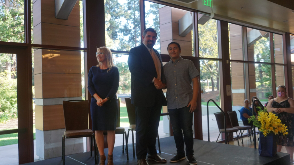 Chief Academic Officer Micah in suit and tie shakes hand with male student at 8th grade graduation on stage in front of crowd