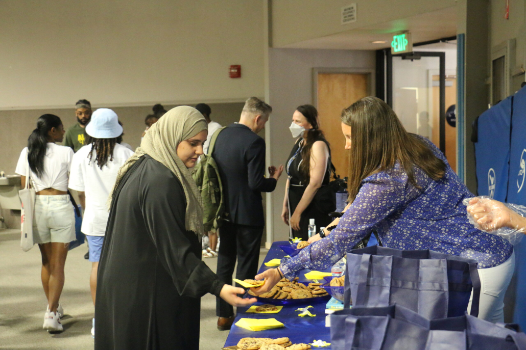 Family event, crowd of people, woman hands another woman a cookie on a napkin