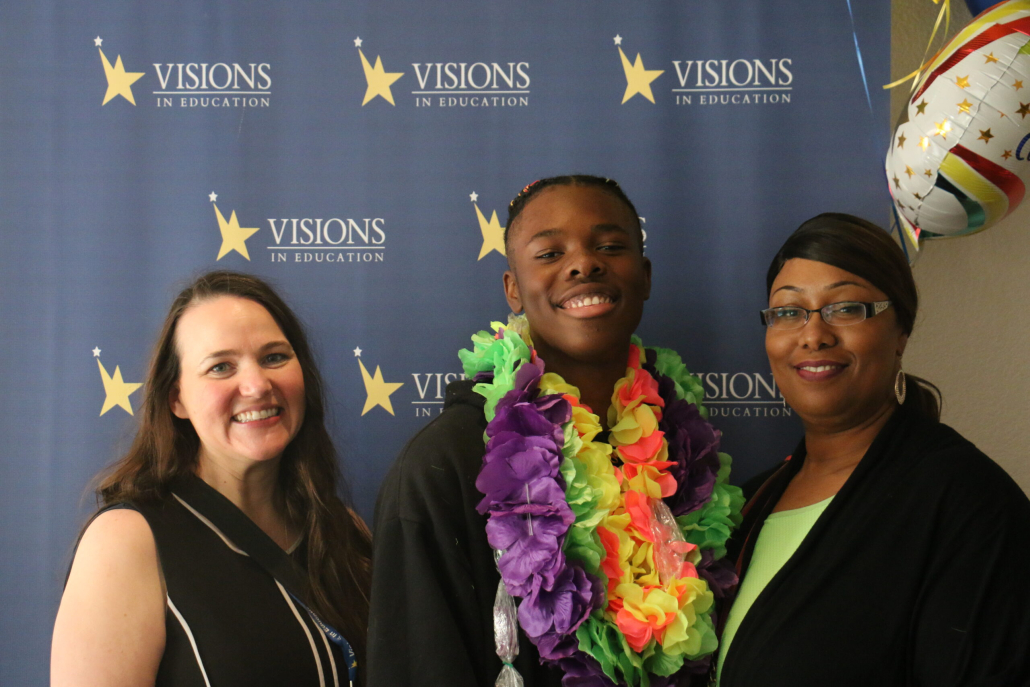 Black male 8th grade student poses with mom and teacher wearing leis at middle school graduation