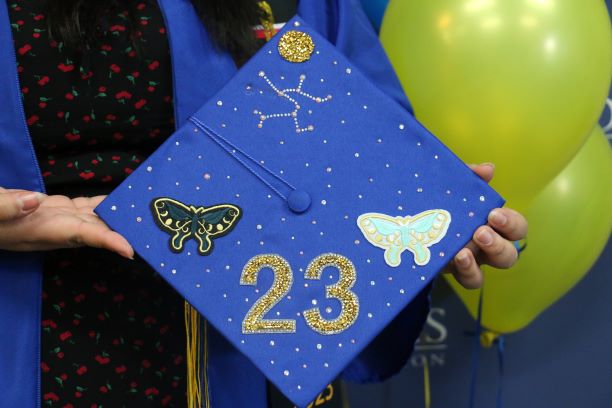 Blue graduation cap decorated with sparkly stickers including moths, a constellation and the number "23"