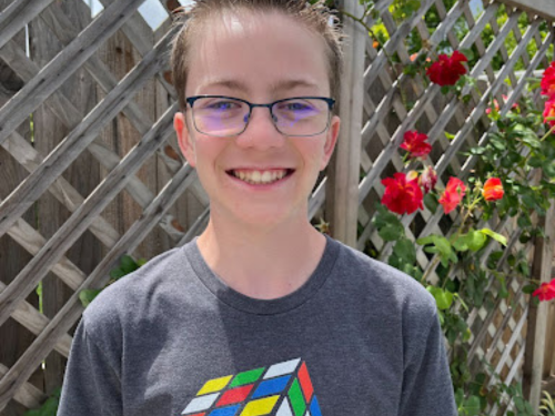 Tyler Hess web High school student smiles for his photo wearing glasses and a shirt with a Rubik's Cube on it