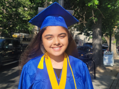Jalissa W web High school girl smiles in bright blue graduation cap and gown wearing yellow tassels at her high school graduation.
