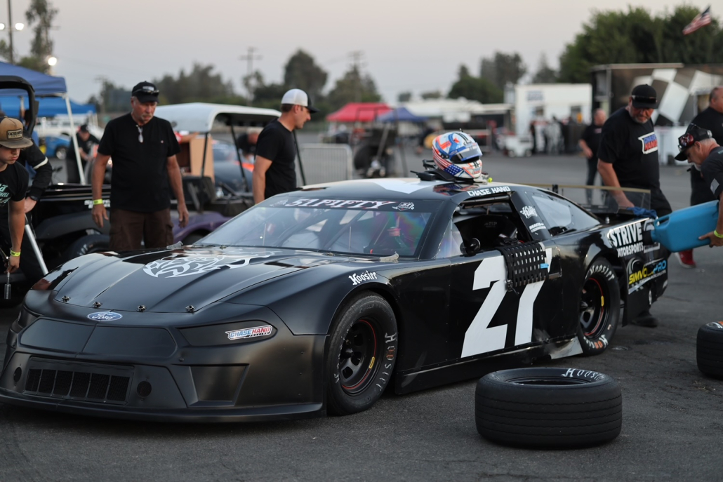 Wearing a helmet, Chase pops his head through the sunroof of his race car with the number 27 on it.