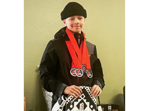 Jax Allen web Jax Allen poses with his snowboard wearing a black beanie, black jacket, and multiple red medals around his neck.