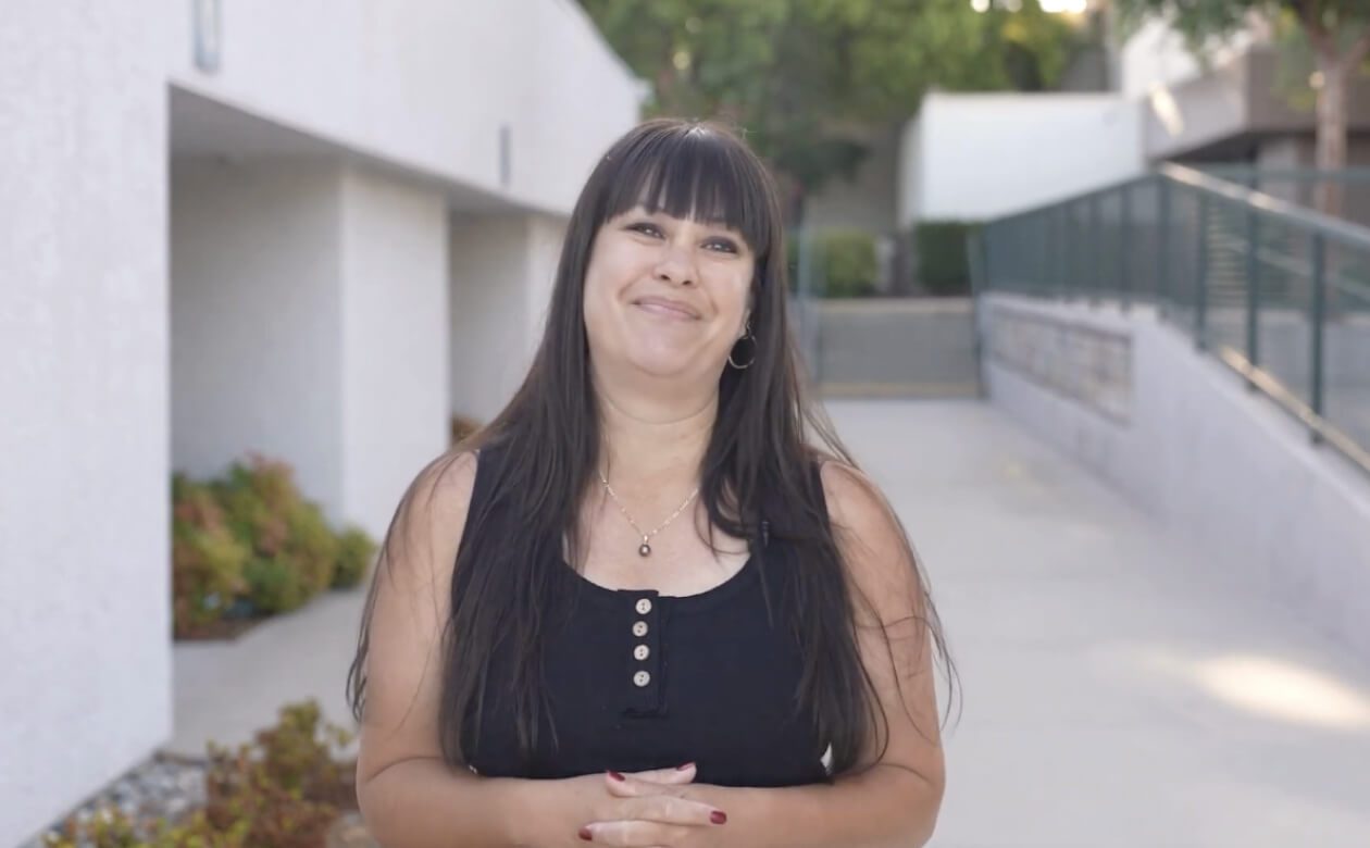 Christine, a teacher, stands confidently in front of a modern building, showcasing her elegance and poise.