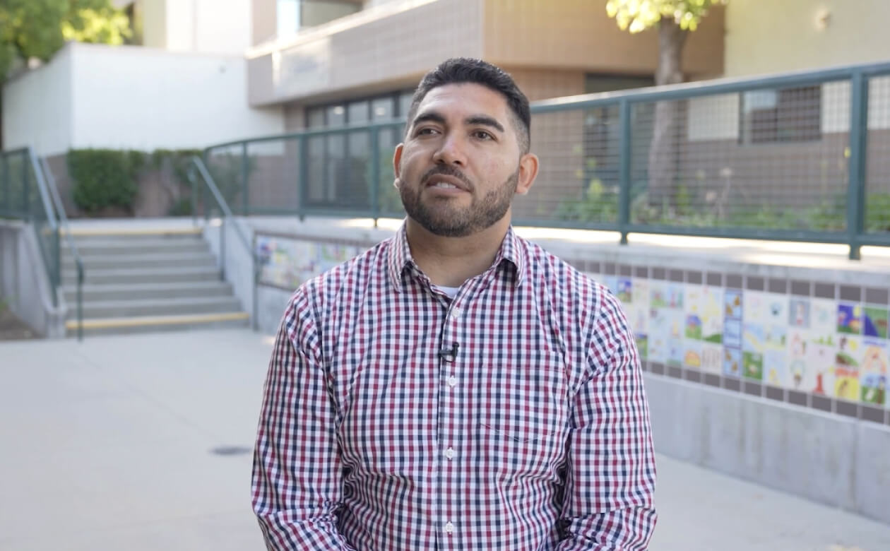 Sergio, a social worker, poses in front of a building, symbolizing the commitment to education emphasized