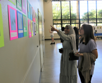 Two young students point at a piece of student artwork on the wall in neon colors.