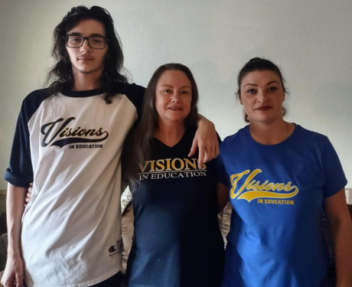 A teenage boy, his grandmother and his mother stand in a row in different Visions In Education shirts and smile for the camera.