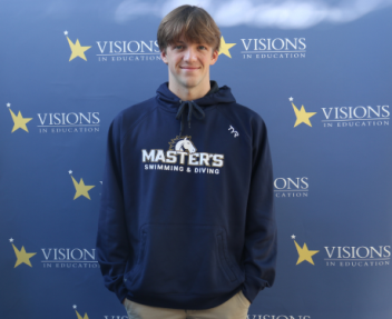 Charley Sears, in a navy The Master's University sweatshirt that reads Master's Swimming and Diving, poses in front of a blue backdrop with Visions In Education logos on it.