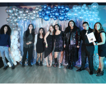 Visions' Coffee House Hangout club gathers together in front of a gray, white, and blue backdrop of streamers and balloons and takes a group photo with their club advisor holding a sign that says "Coffee House Club".