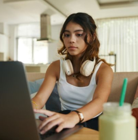 Serious teenage girl with headphones working on laptop on her online high school cybersecurity college class