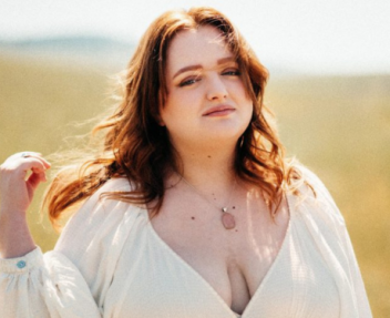 Redheaded high school female in a white dress poses in an open field for graduation pictures