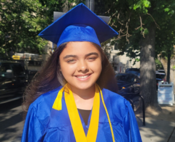 High school girl smiles in bright blue graduation cap and gown wearing yellow tassels at her high school graduation.
