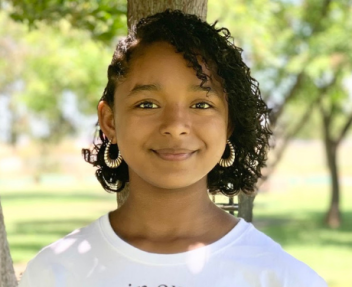 Mikaela, a teen student that owns her own business, smiles at the camera in a park