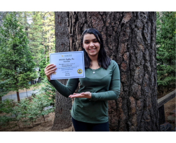 8th grader Elissa winner of 2020 spelling bee poses with certificate in front of large tree