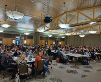 Over 250 Visions staff sits around multiple tables in a big community center room and smiles for a group photo.