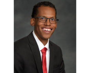 Board Member Terrence Shelton, in a black jacket, white shirt, and red tie smiles, poses for a portrait photo.