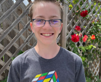 High school student smiles for his photo wearing glasses and a shirt with a Rubik's Cube on it