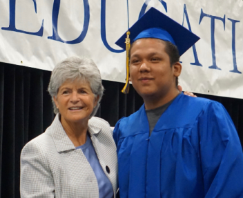 Summer grad posing on stage with Superintendent Jody Graf