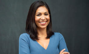 A woman in a blue dress smiles warmly at the camera, exuding joy and confidence.