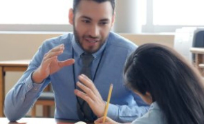 A teacher tutoring a student as she jotting down notes with a pencil and paper while seated