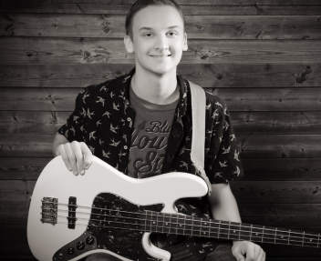 Male student smiling at the camera holding a guitar