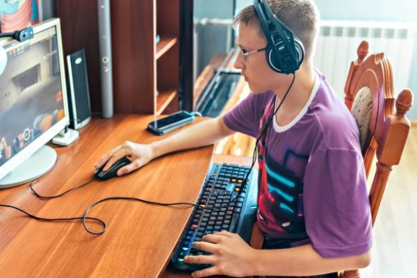 A teenage boy, a young man playing and creating video games on a computer, using technology, wearing headphones, using a computer.