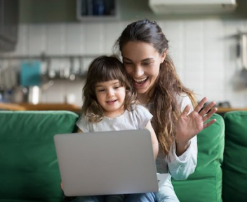 Happy mother and kid daughter waving hands looking at web camera using laptop for video call