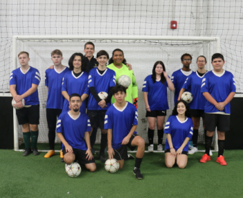 Visions' club soccer team huddles together in front of a soccer goal post for a team photo.