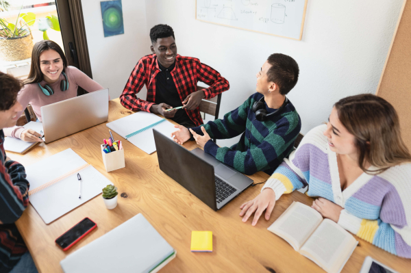 A diverse group of people collaborating around a table, each focused on their laptops, sharing ideas and working together.